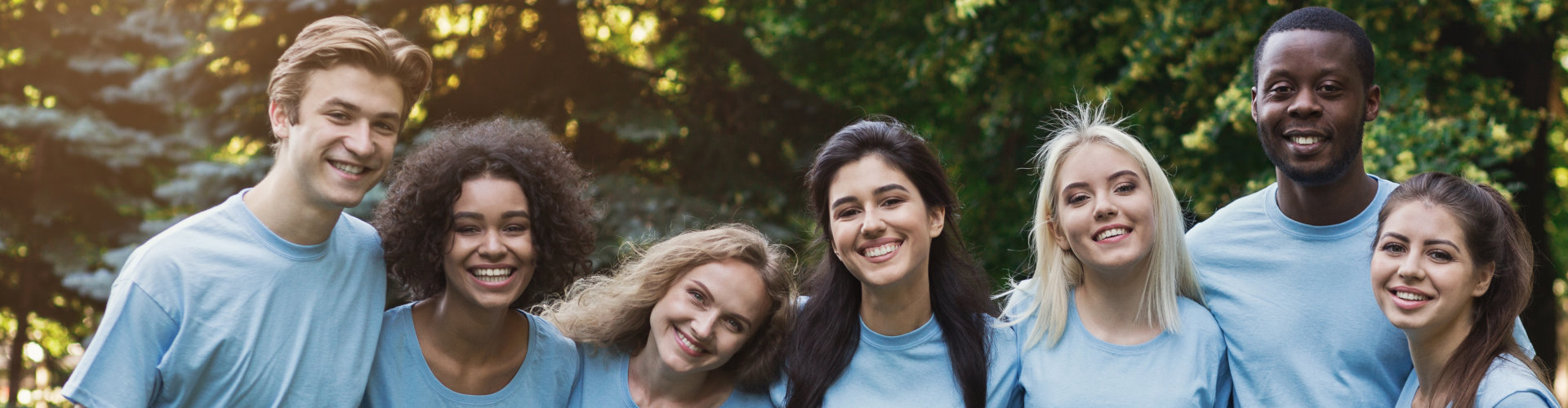 Group of happy young diverse volunteers embracing at park